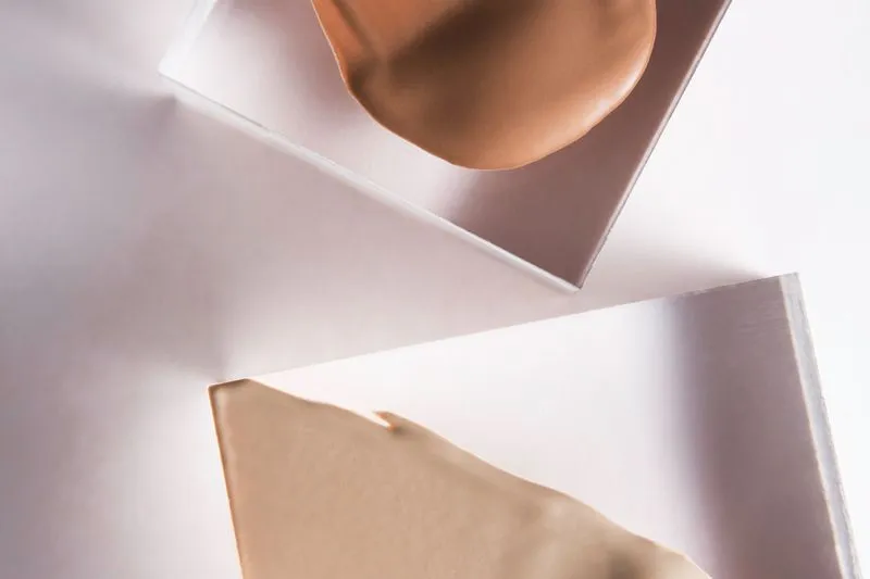 Deux touches de fond de teint liquide, une beige et une caramel, étalées sur des blocs transparents