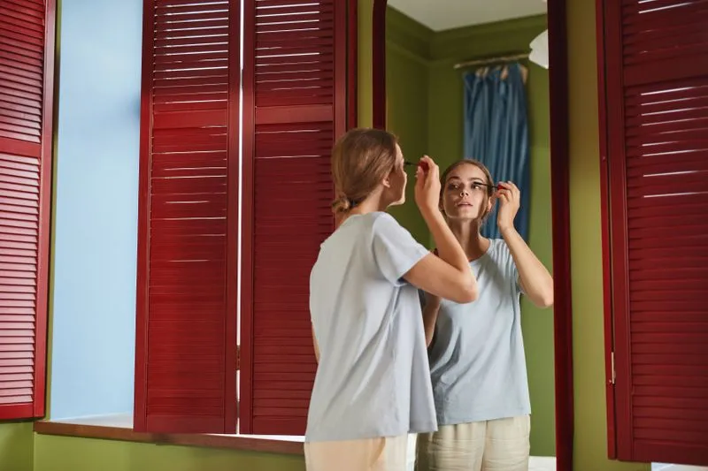 Jeune femme qui passe la brosse de mascara sur ses cils face à un miroir
