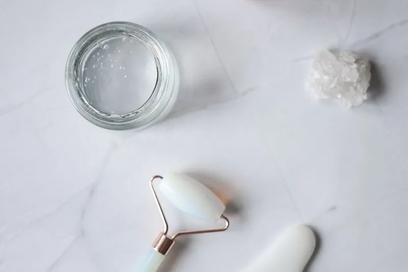 Pot en verre ouvert rempli d'un gel transparent, posé sur du marbre à côté d'un rouleau de massage