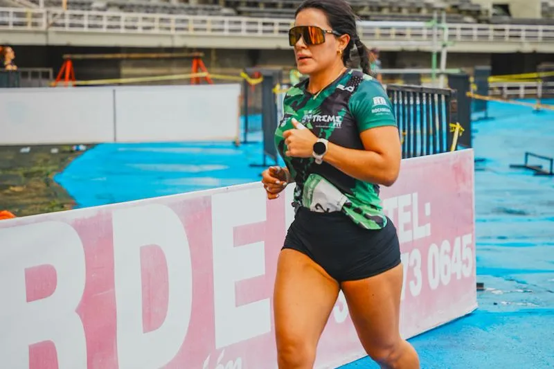 Coureuse sur une piste de stade, en t-shirt de sport vert et noir, qui porte de larges lunettes de soleil de sport enveloppantes