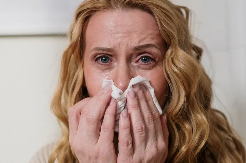 Femme aux yeux rougis et larmoyants qui presse un mouchoir en papier contre son nez