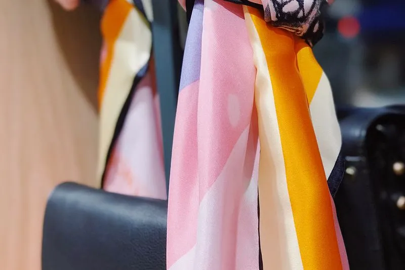 Foulard en soie à rayures rose, orange et crème noué sur un sac à main en cuir noir