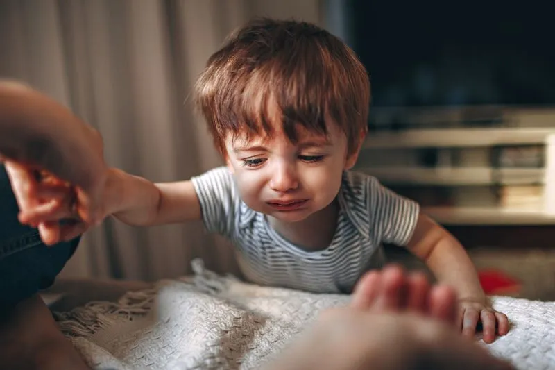Petit garçon en larmes, la bouche tordue par les pleurs, qui tend le bras vers la main d'un adulte