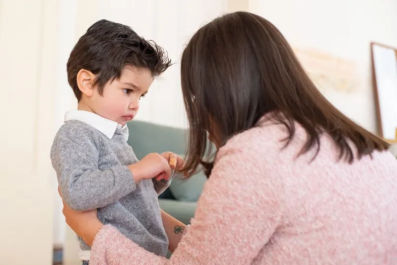 Mère penchée à hauteur d'un petit garçon dans un salon, qui lui parle doucement pendant qu'il baisse les yeux