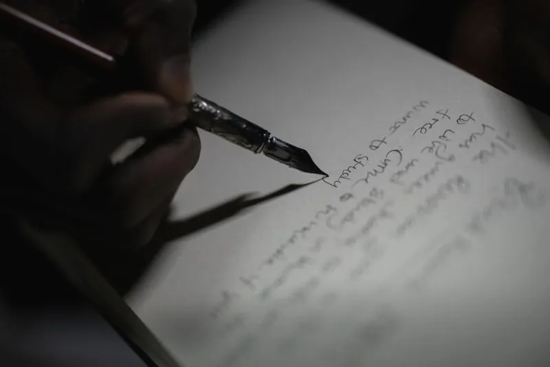 Gros plan sur une main qui écrit quelques lignes à la plume sur une page blanche