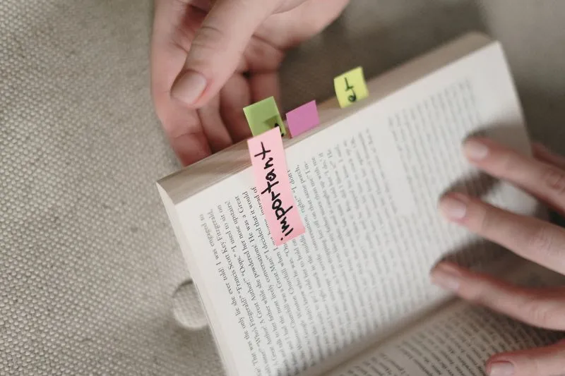 Roman ouvert tenu à deux mains, marqué de petits Post-it colorés dont un rose sur lequel est écrit « important »