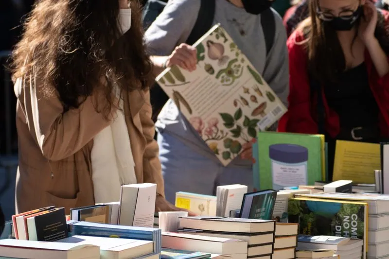 Visiteuses qui feuillettent des livres autour d'une table de salon du livre en plein air, romans et beaux livres empilés