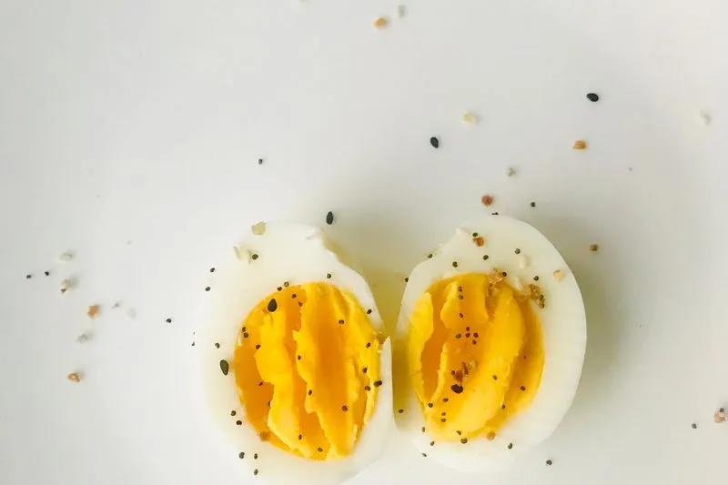 Deux moitiés d'œuf dur au jaune bien pris, parsemées de graines, sur un fond blanc