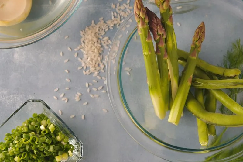Asperges vertes dans un saladier en verre et oignons nouveaux émincés dans un ramequin, sur un plan de travail