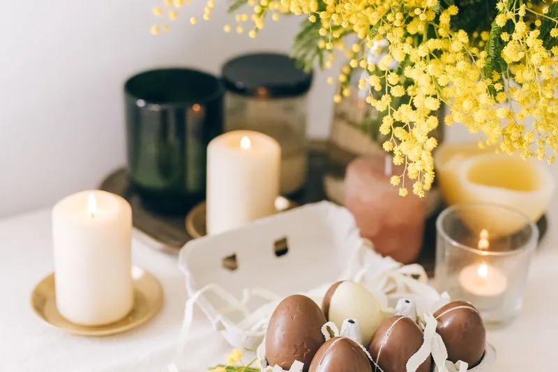 Bouquet de mimosa, bougies allumées et œufs en chocolat dans une boîte à œufs, sur une nappe blanche