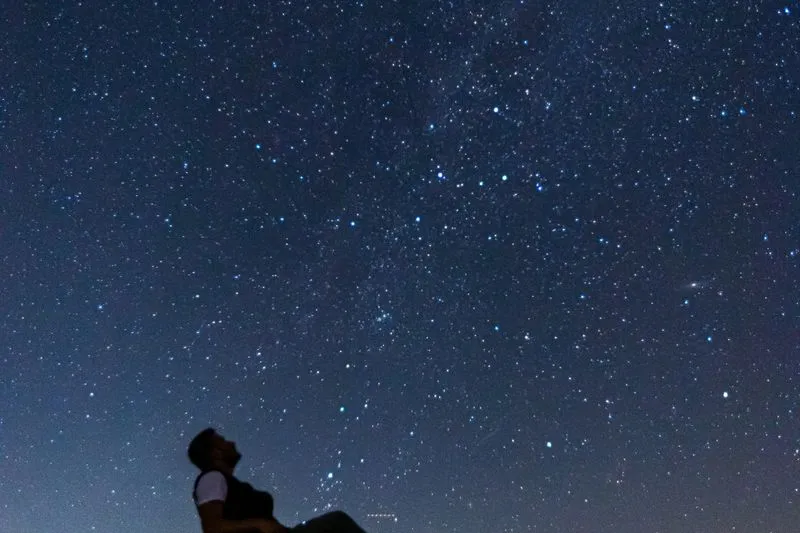 Silhouette d'un homme renversé en arrière qui contemple un ciel nocturne constellé d'étoiles