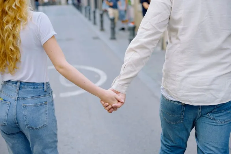 Couple vu de dos qui marche main dans la main dans une rue piétonne, elle en tee-shirt blanc, lui en chemise de lin