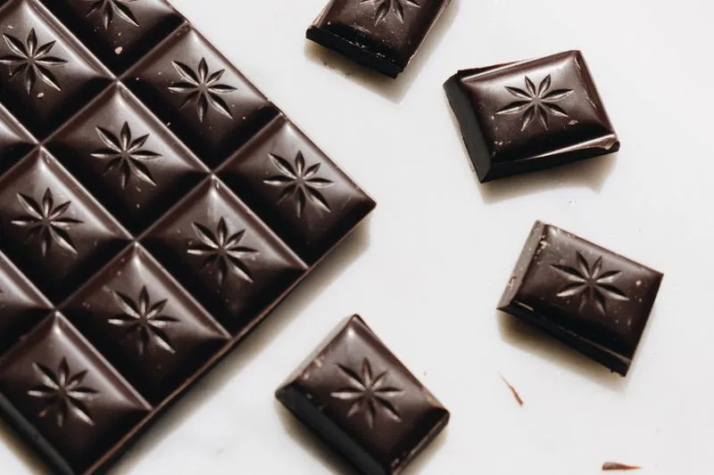 Tablette de chocolat noir et carrés détachés sur une surface blanche