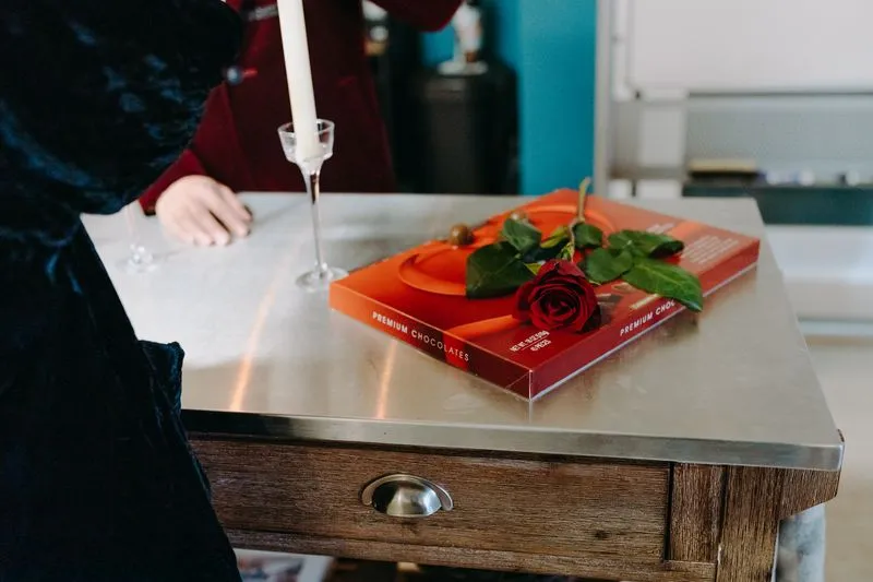 Coffret rouge de chocolats avec une rose rouge posée en travers, près d'un bougeoir