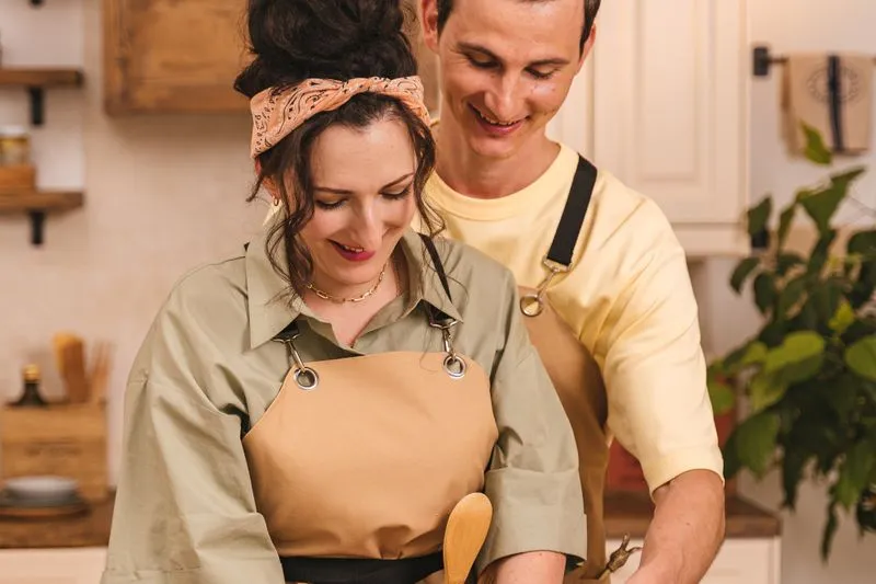 Couple en tablier qui cuisine côte à côte en souriant