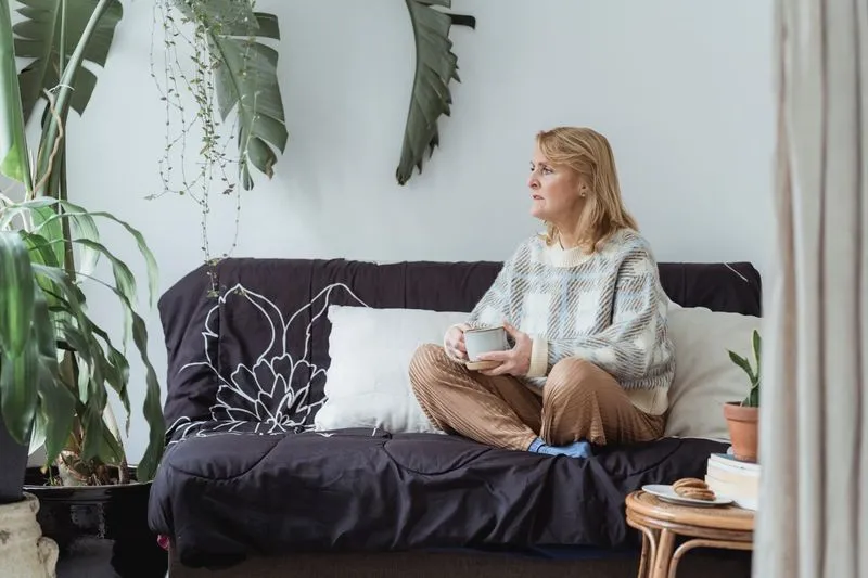 Femme d'une cinquantaine d'années assise en tailleur sur un canapé, une tasse entre les mains