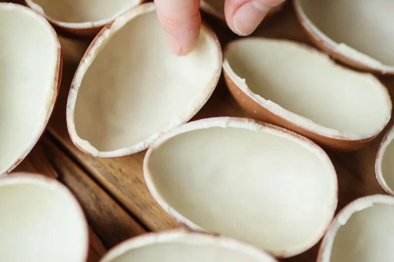 Demi-coques d'œufs de Pâques en chocolat au lait posées sur une table en bois, qu'une main met en place