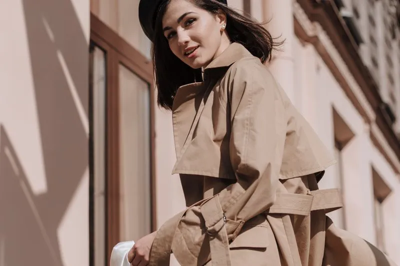 Femme en béret noir dans un trench beige : cape sur les épaules, ceinture et boucle en métal à la taille