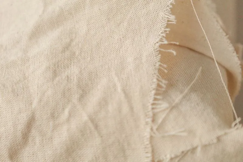 Gros plan sur une toile de coton écrue au bord effiloché, dont la trame se voit à l'œil nu
