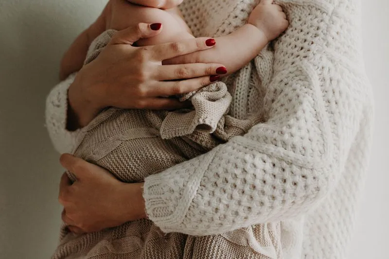 Mère qui serre contre elle son bébé emmitouflé dans une couverture en maille