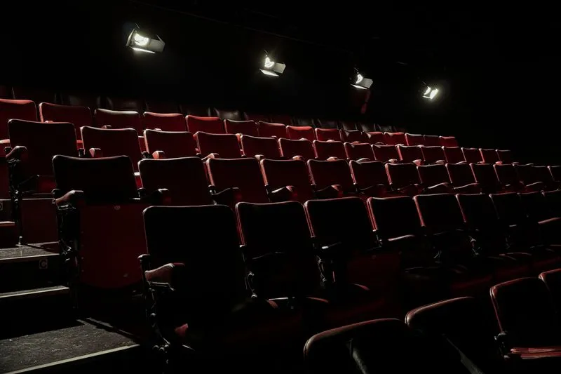 Rangées de fauteuils rouges vides disposés en gradins, éclairées par quatre projecteurs suspendus