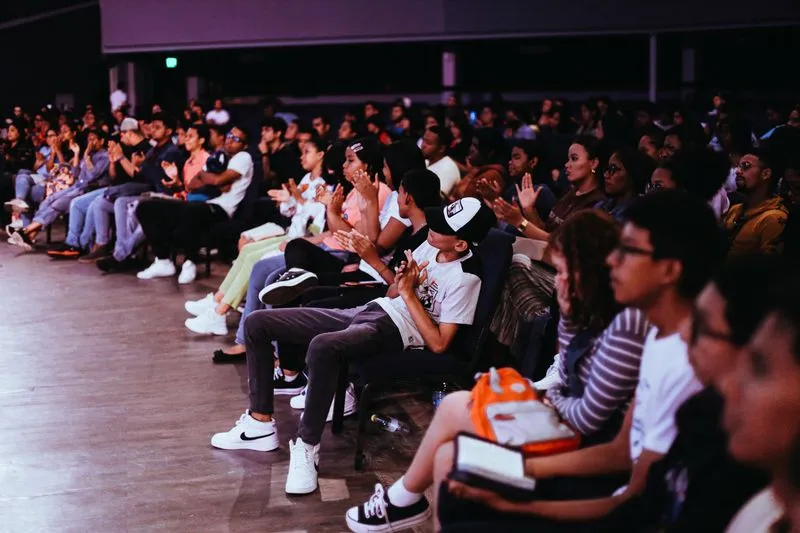 Rangées de jeunes spectateurs assis qui applaudissent dans une salle à la lumière tamisée