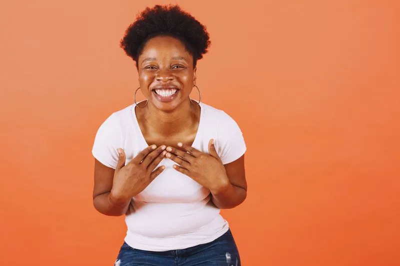 Jeune femme rieuse en tee-shirt blanc uni et jean, devant un fond orange