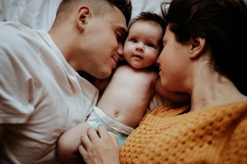 Jeune couple allongé sur un lit, joue contre joue avec leur bébé couché entre eux