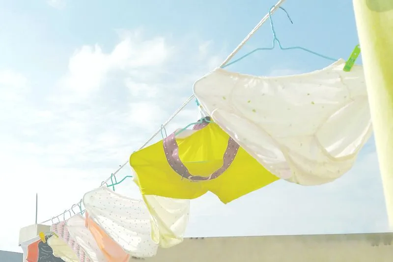 Culottes en coton blanches, jaunes et roses suspendues à une corde à linge sous un ciel bleu