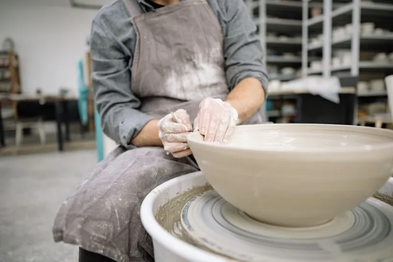 Mains couvertes d'argile qui façonnent un grand bol sur un tour de potier, dans un atelier de céramique