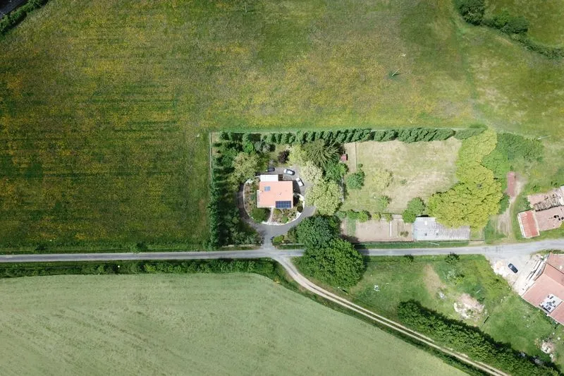 Vue aérienne d'une maison de campagne entourée d'un jardin clos de haies, au milieu des champs