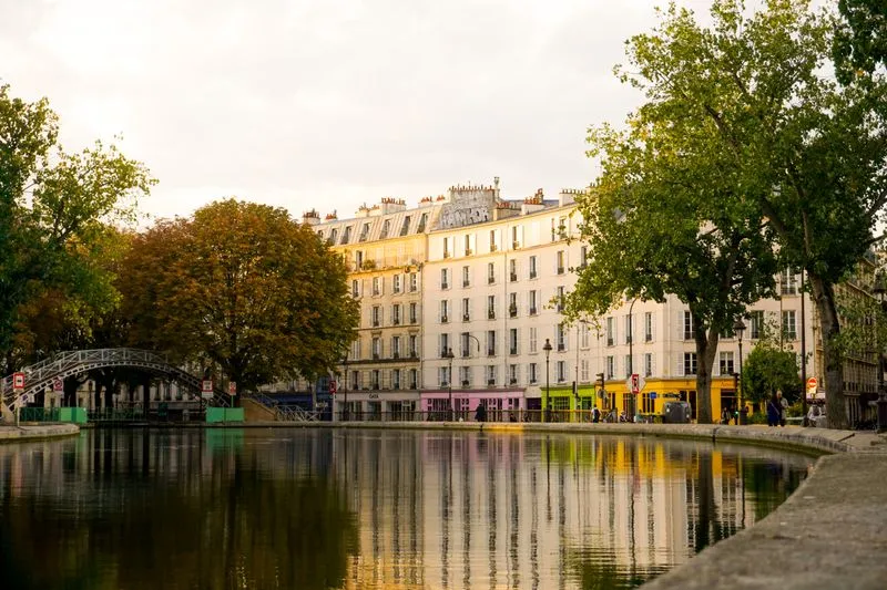 Quai du canal Saint-Martin en fin de journée, une passerelle métallique à gauche et des immeubles clairs qui se reflètent dans l'eau