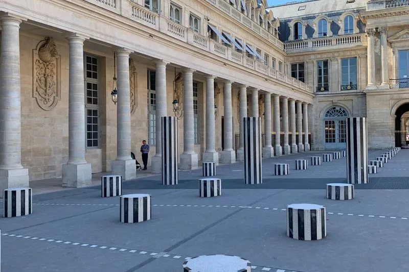 Colonnes rayées noir et blanc de différentes hauteurs dans la cour du Palais-Royal, devant une galerie de colonnes en pierre