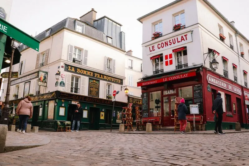 Carrefour pavé de Montmartre avec le restaurant Le Consulat à la façade rouge et La Bonne Franquette à la façade verte
