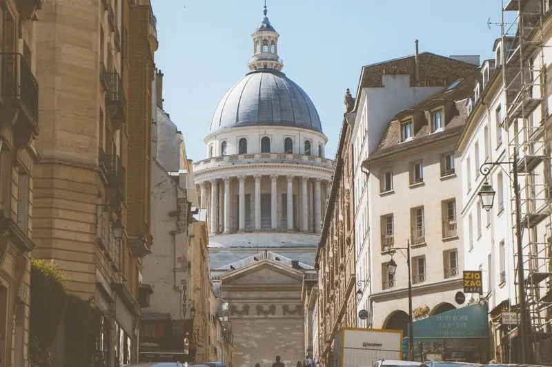 Rue du Quartier latin bordée d'immeubles en pierre de taille, le dôme du Panthéon au bout sous un ciel bleu