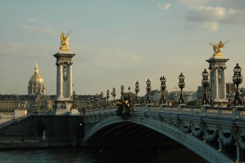 Pont Alexandre-III à Paris avec ses candélabres ouvragés et ses statues dorées, le dôme des Invalides au fond, la Seine au premier plan en fin de journée