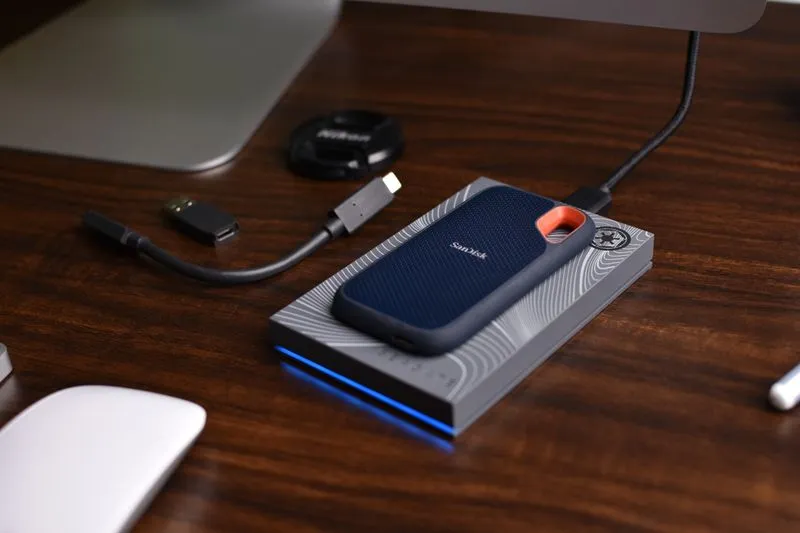SSD portable posé sur un disque dur externe, avec son câble USB-C, sur un bureau en bois sombre