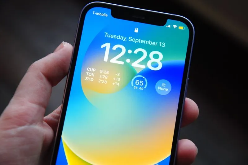 Main qui tient un iPhone allumé sur l'écran de verrouillage, heure et widgets affichés