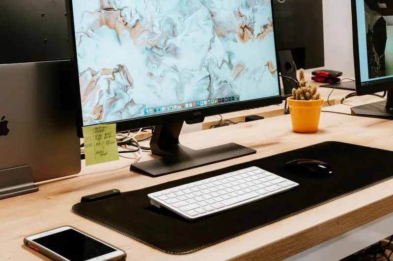 Bureau en bois avec un écran, un ordinateur portable fermé sur son support et un smartphone posé devant le clavier