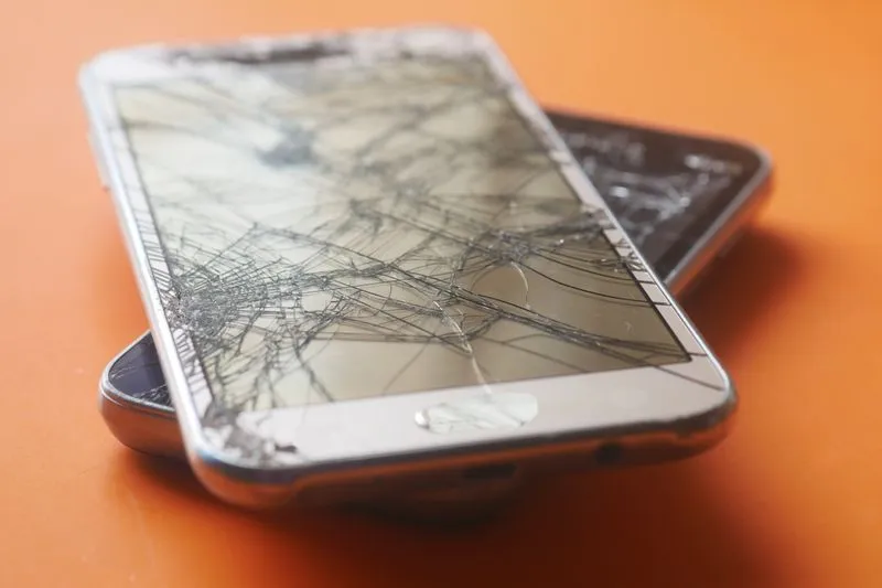 Deux smartphones à l'écran brisé, empilés sur une surface orange
