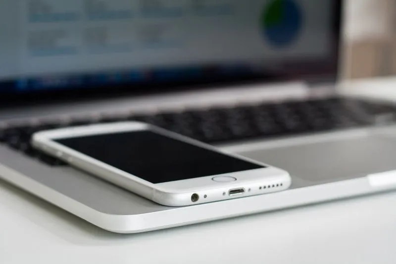 iPhone blanc posé sur le repose-poignets d'un ordinateur portable ouvert