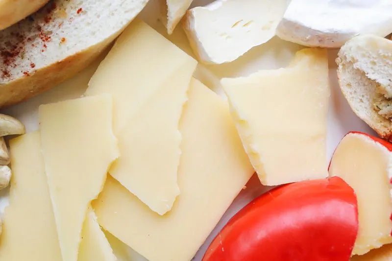 Gros plan sur un assortiment de fromages en tranches, avec quelques morceaux de pain