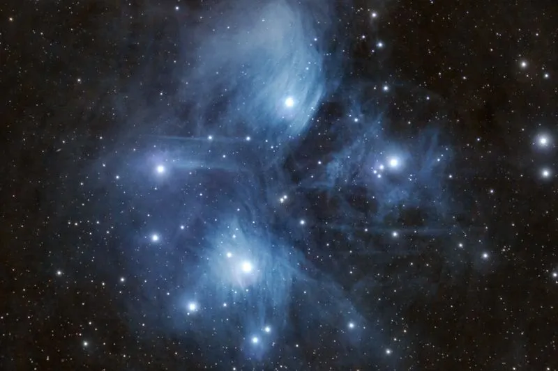 Les Pléiades, amas d'étoiles bleutées enveloppées d'un voile de nébulosité, sur fond de ciel étoilé