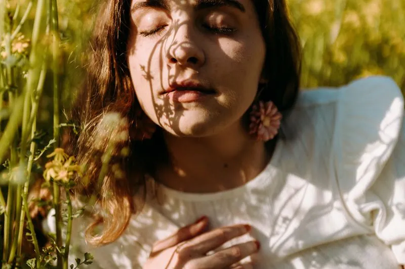 Jeune femme allongée dans les herbes hautes, les yeux fermés, le visage strié d'ombres de fleurs au soleil