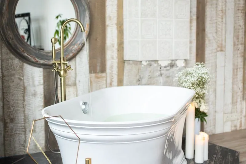 Baignoire blanche qui se remplit sous un robinet en laiton, entourée de bougies et d'un bouquet de gypsophile