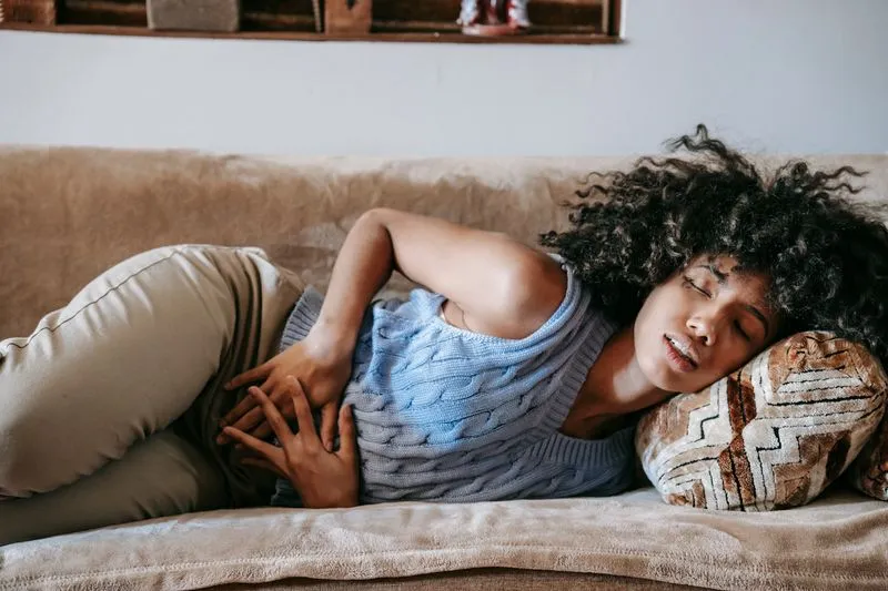 Femme allongée sur un canapé, les mains posées sur le ventre, le visage crispé par la douleur