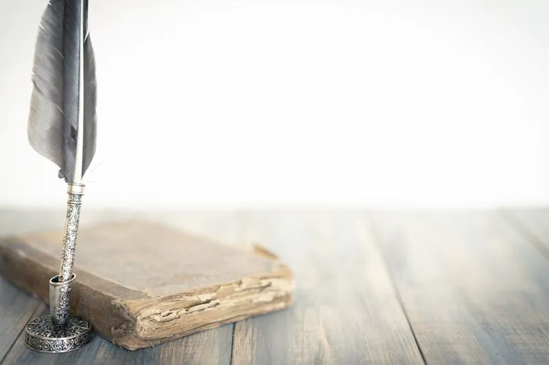 Vieux livre relié à la couverture usée, posé sur une table en bois à côté d'une plume d'écriture