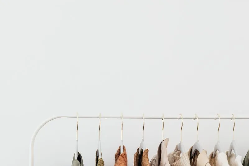 Portant blanc où pendent des vêtements aux tons neutres, du sauge au rouille en passant par le beige et le crème