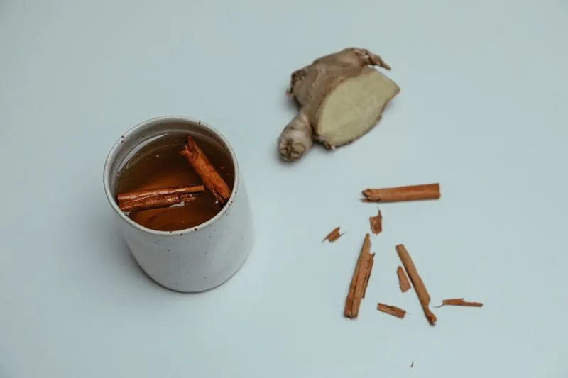 Racine de gingembre fraîche coupée en deux, à côté d'une tasse d'infusion et de bâtons de cannelle