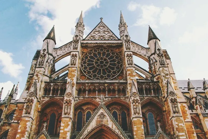 La façade gothique de l'abbaye de Westminster et sa grande rosace, vues en contre-plongée sous un ciel bleu traversé de nuages